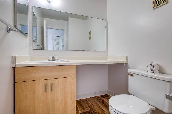 A bathroom with a toilet next to a sink and long countertop at Wood Creek Apartments, Kenosha