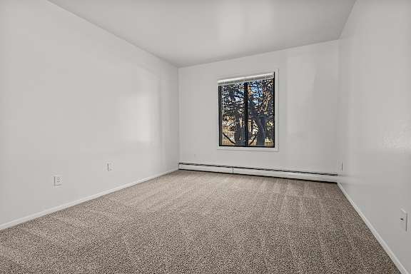 A bedroom with a carpeted floor and a window showing trees outside at Wood Creek Apartments, Kenosha
