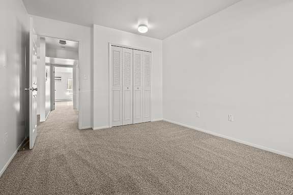 A bedroom with a carpeted floor and a large closet at Wood Creek Apartments, Kenosha