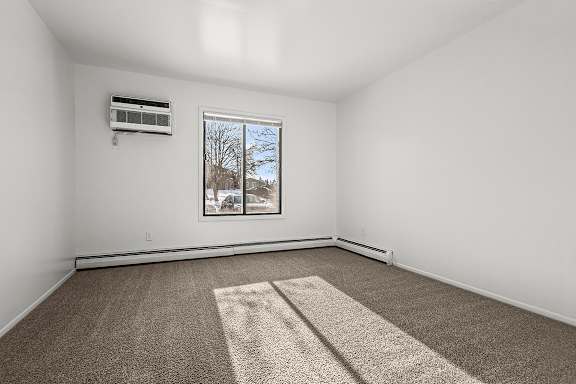 A large primary bedroom with a carpet, a window, and an air conditioner at Wood Creek Apartments, Kenosha