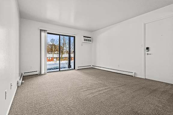 A living room with a carpeted floor and a sliding glass door leading to a patio at Wood Creek Apartments, Kenosha