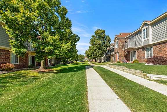A grassy courtyard with trees and a sidewalk at Wood Creek Apartments, Kenosha