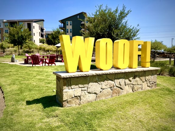 a large yellow sign that says woof in the middle of a grassy area