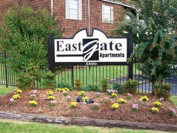 East Gate Monument sign with gate surrounding the community. Flowers are in front of the sign and two trees are next to it.