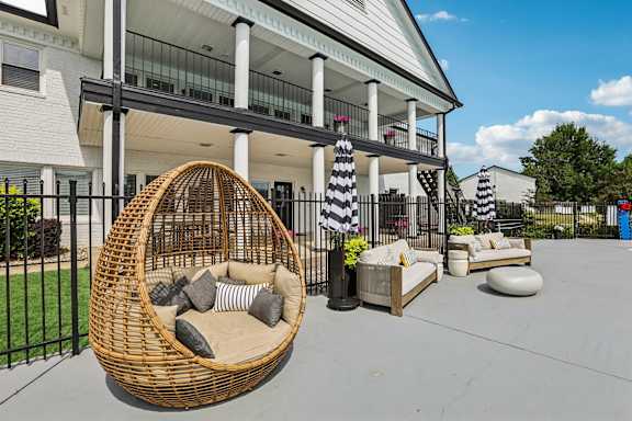 A wicker chair with cushions is in the foreground of a patio area.