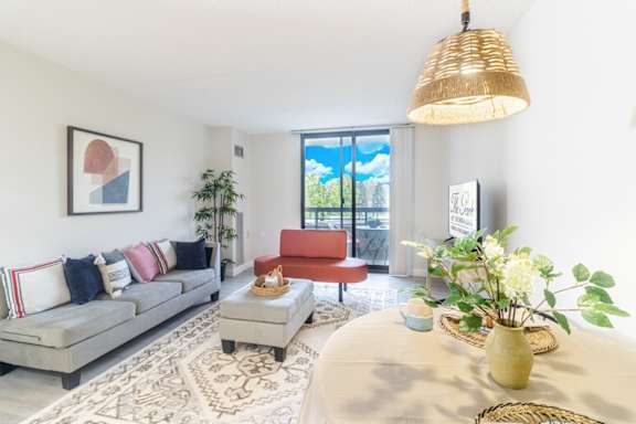 A living room with a grey couch, a red chair, a coffee table, and a large window with a view of the trees outside.
