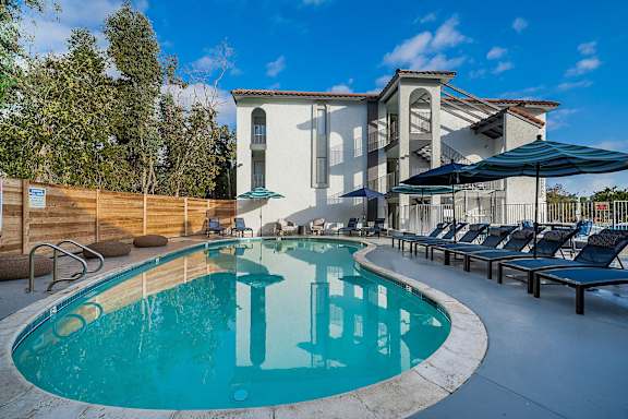 A large outdoor swimming pool with lounge chairs and a building in the background.