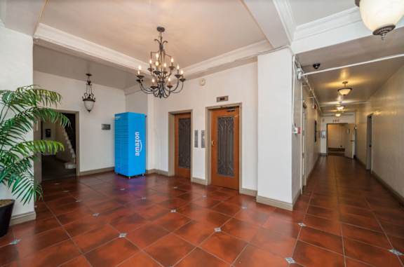 A blue recycling bin sits in the middle of a room with a chandelier hanging from the ceiling.