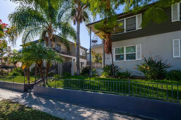 A residential area with a house, palm trees, and a metal fence.