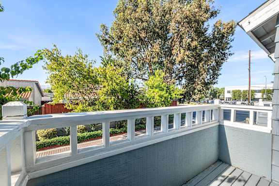 A balcony with a white railing and a view of trees and buildings.