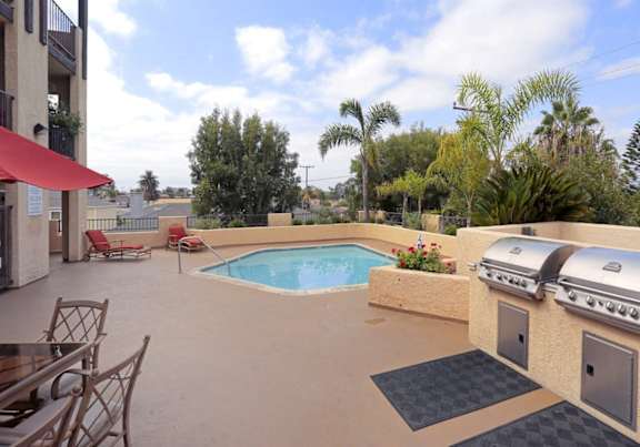 a backyard with a pool and a patio with chairs and a grill
