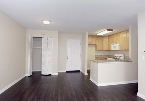 an empty living room and kitchen with wood flooring and white walls