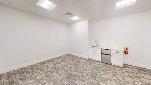 A white room with a grey carpet and a fridge.