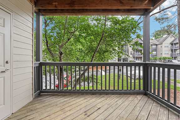 A wooden deck with a white door and a view of a street and trees.