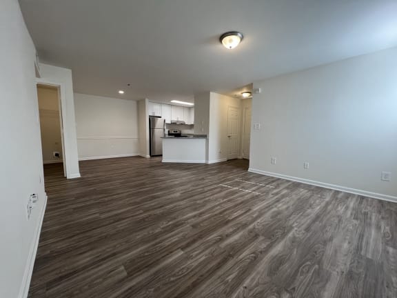an empty living room with wood flooring and a kitchen