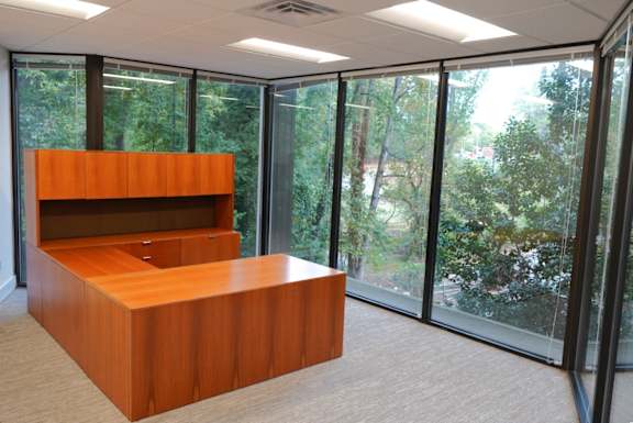 A wooden desk with a shelf and drawers is in a room with large windows.