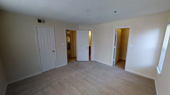 A room with white walls and carpeted floor with three doors.