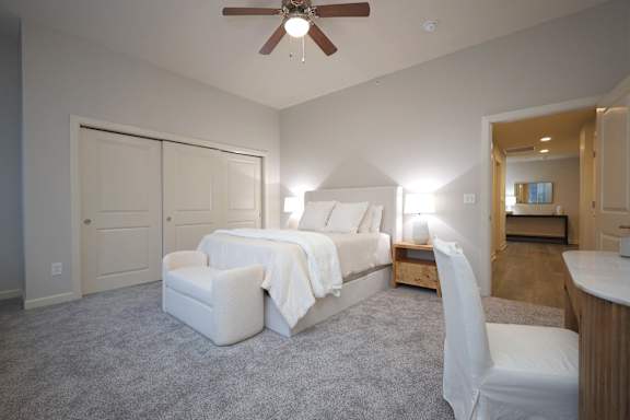 A bedroom with a bed, chair, and a ceiling fan.