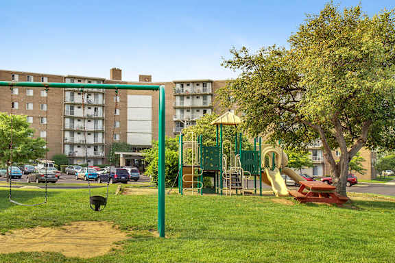 A playground with a green swing set and a red slide in front of apartment buildings.