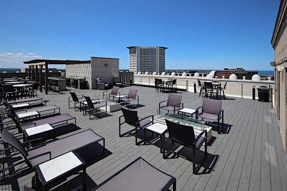 A rooftop patio with chairs and tables overlooking a cityscape.