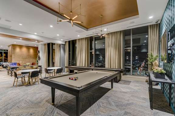 A pool table is in the middle of a room with a wooden floor and a glass wall.