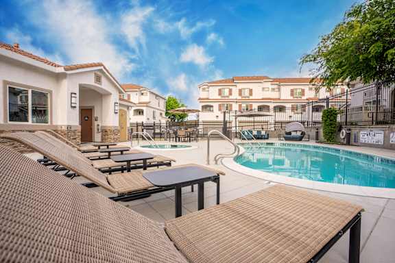 A pool area with sun loungers and a building in the background.