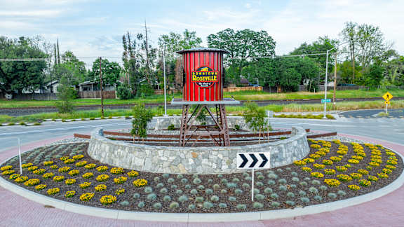 A red and black sign on a pole in the middle of a flowerbed.