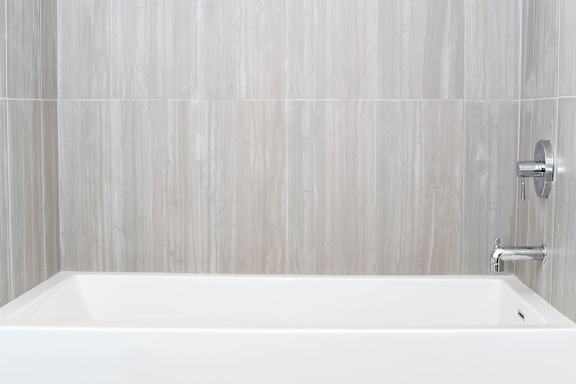 A white bathtub in a bathroom with grey tiled walls at Wilshire Valencia Apartment, Los Angeles, CA, 90017