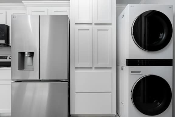 A stainless steel refrigerator stands next to a white washing machine in a kitchen.