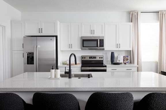 A kitchen with a white countertop and black chairs.