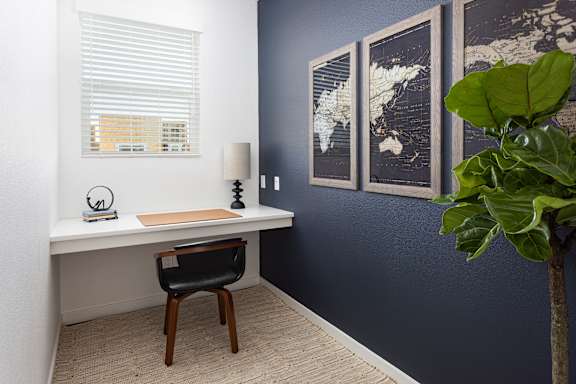 A room with a desk, chair, and a potted plant.