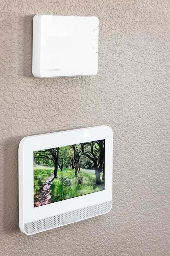 A wall-mounted device with a screen displays a picture of a pathway through a wooded area.