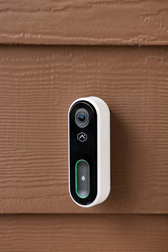 A white smart device with a camera and two buttons is mounted on a brown wooden surface.