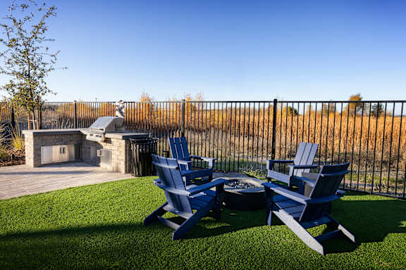 Two blue chairs are on a lawn in front of a fireplace.