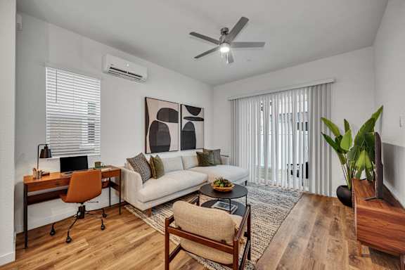 A living room with a couch, a chair, a desk, and a ceiling fan.