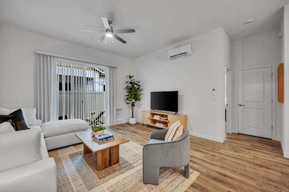A living room with a white couch, a wooden coffee table, and a television on a stand.