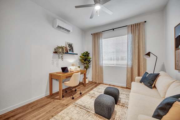 A room with a desk, a couch, and a ceiling fan.