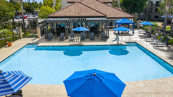 A pool with blue umbrellas and chairs. at 55+ FountainGlen Grand Isle, Murrieta California