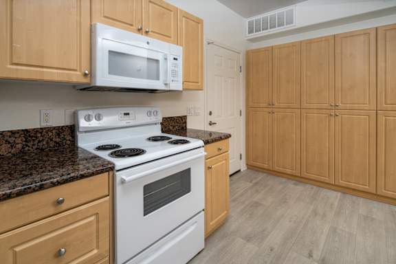 Minimal kitchen with brown wood cabinets at 55+ FountainGlen Grand Isle, Murrieta, 92562