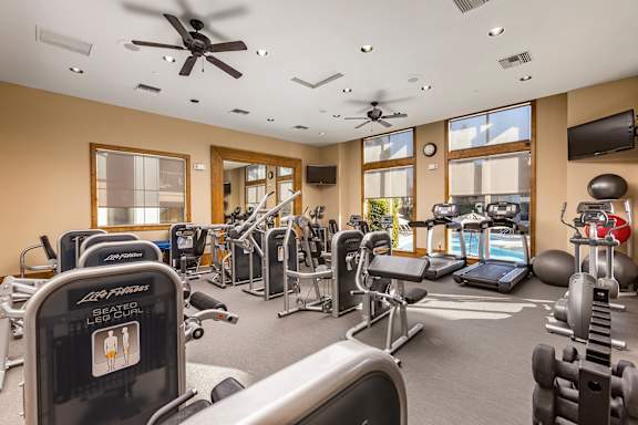A gym with a variety of equipment including treadmills, weights, and exercise machines at 55+ FountainGlen  Jacaranda, California