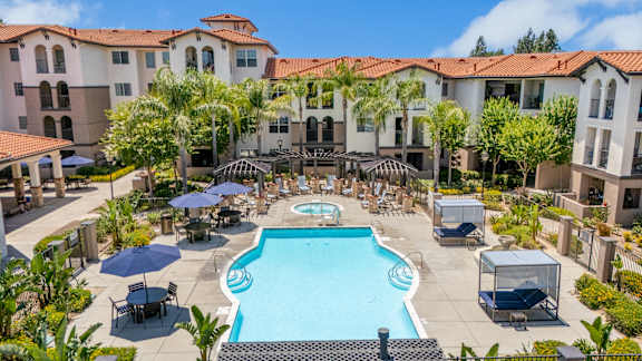 A large swimming pool surrounded by lounge chairs and umbrellas in a resort-like setting. at 55+ FountainGlen Terra Vista, Rancho Cucamonga, CA
