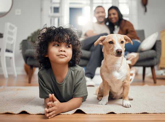 A young child and a dog are sitting on a rug in a living room.