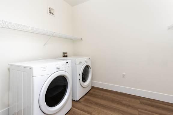 Two white front loading washing machines in a laundry room at Miro at the Parc Apartments, Henderson