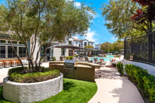 A well-maintained garden with a circular stone planter in the foreground and a pool area in the background.