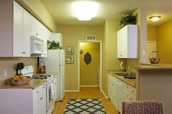 A kitchen with white cabinets and appliances, a black and white rug on the floor, and a yellow wall.
