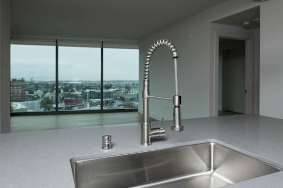 A modern kitchen with a stainless steel sink and a large window overlooking a cityscape.