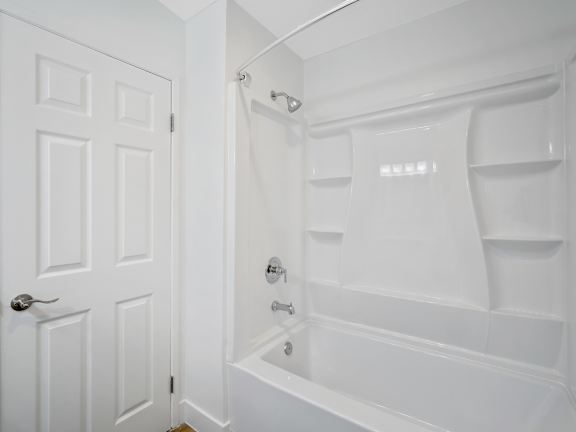 A white bathroom with a door and a bathtub at Verandas Apartments, California