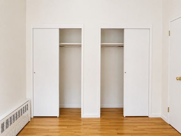 Two white doors in a room with wood floors.