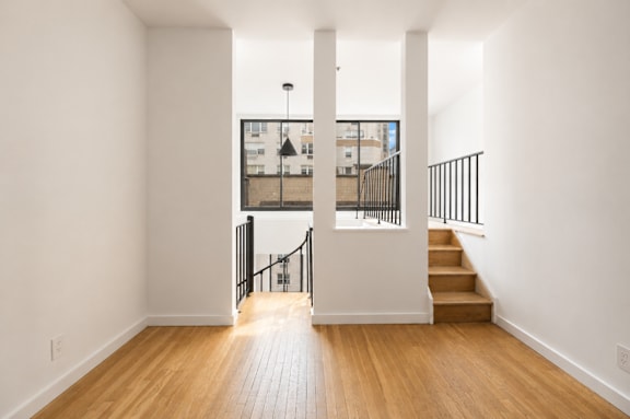 A hallway with wooden floors and a staircase leading to a balcony.