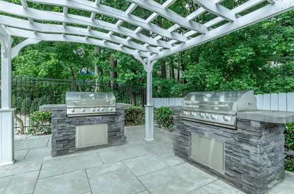 A patio with two stone BBQs under a white pergola at Crest at East Cobb Apartments, GA, 30062